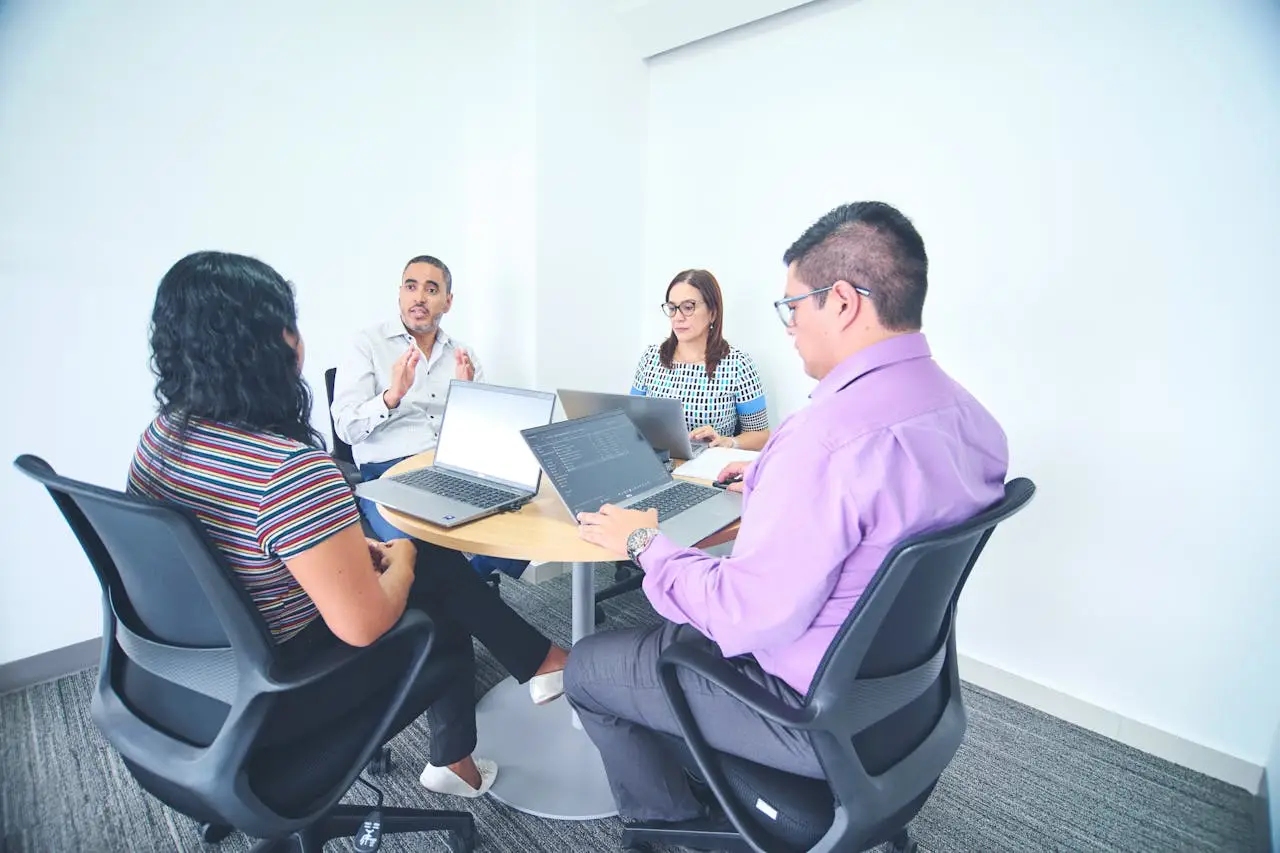 about-07 Diverse team engaged in a corporate meeting with laptops in a bright, modern office setting.