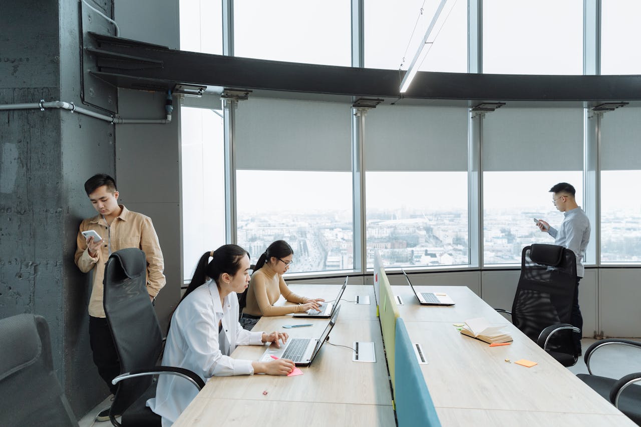 Contemporary office scene with Asian coworkers working on laptops and smartphones.
