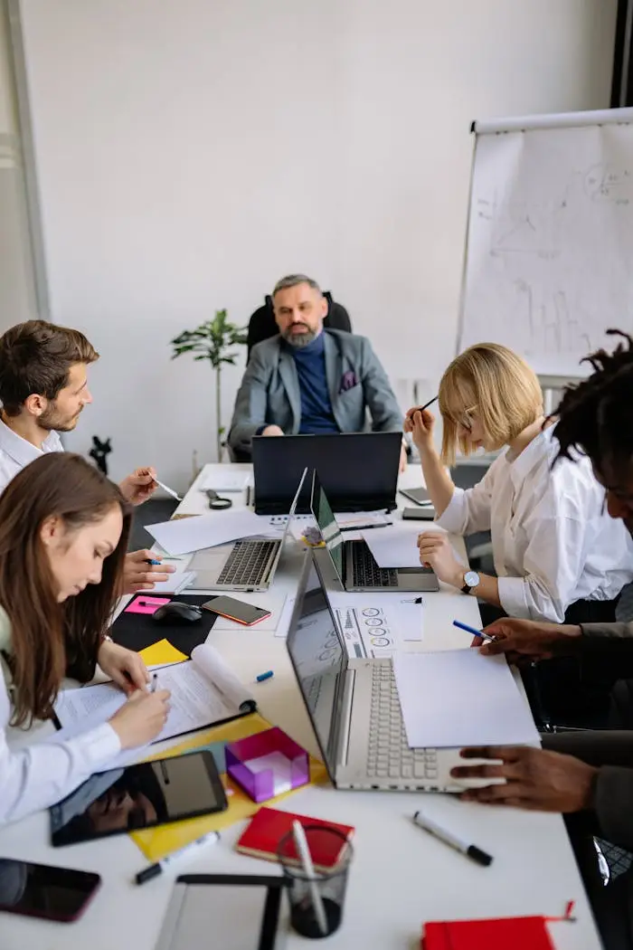 Group of colleagues brainstorming and planning in a modern office with laptops and documents.