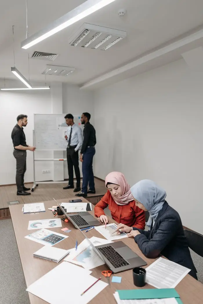 A diverse team collaborates around a table with laptops in an office setting.