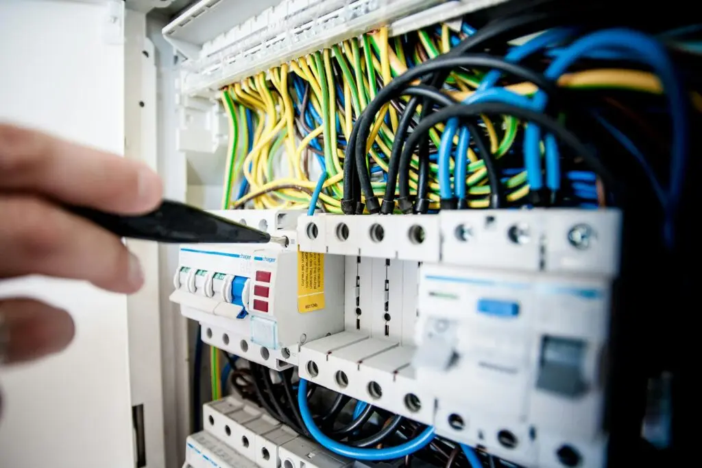 Training & Courses Hand of electrician working on a circuit breaker panel with colorful wires, ensuring safe electrical connections.