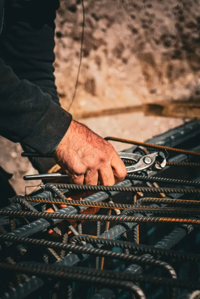 Training & Courses Close-up of a worker's hand using a tool to handle rebar at a construction site, showcasing rugged labor.