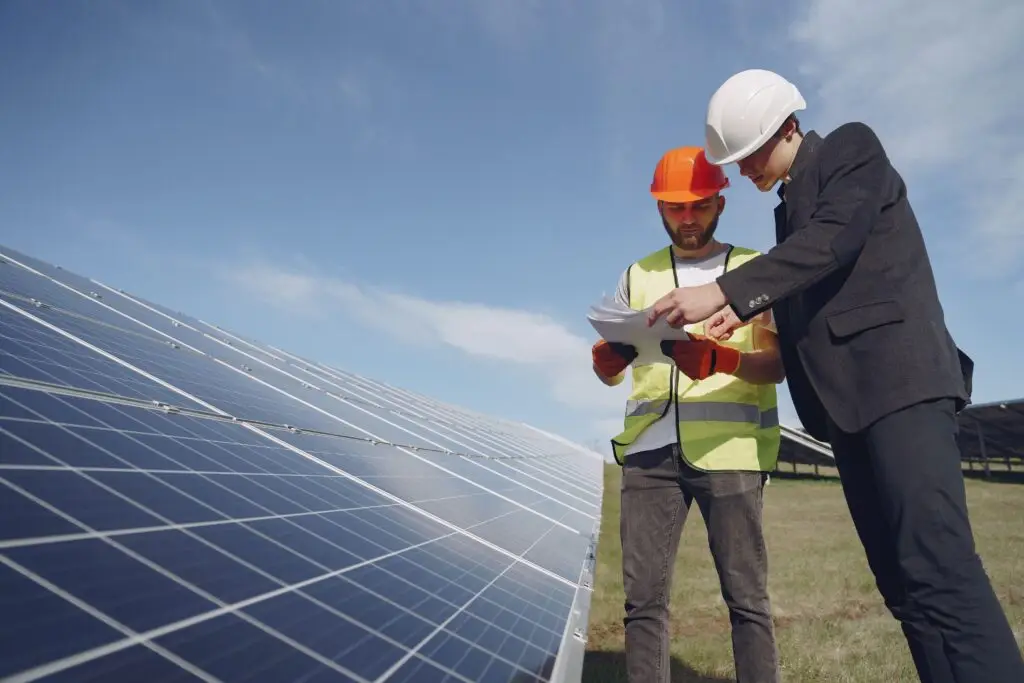 Training & Courses Low angle of young inspector and foreman in hardhats checking documentation against modern solar panels in field
