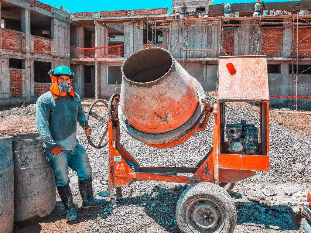 Training & Courses A construction worker operating a concrete mixer at an active building site, emphasizing safety gear.