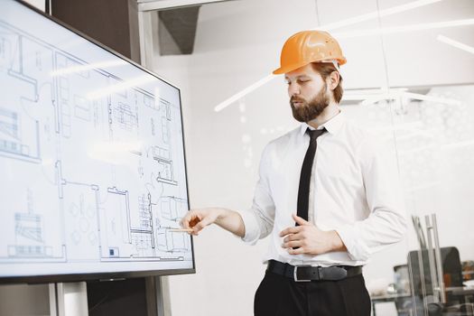 Digital Project Management Professional Programme-(FULL DETAILS) Architect in hard hat reviewing blueprints on a screen, discussing plans in modern office.